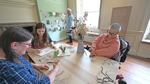 Several people sat around a table sketching surrounded by artwork and inspiration